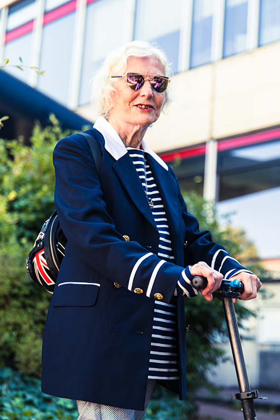 Veste de tailleur, marinière , lunette de soleil, une personne âgée pose tout sourire sur sa trottinette devant la mairie du 8e arrondissement - 1 